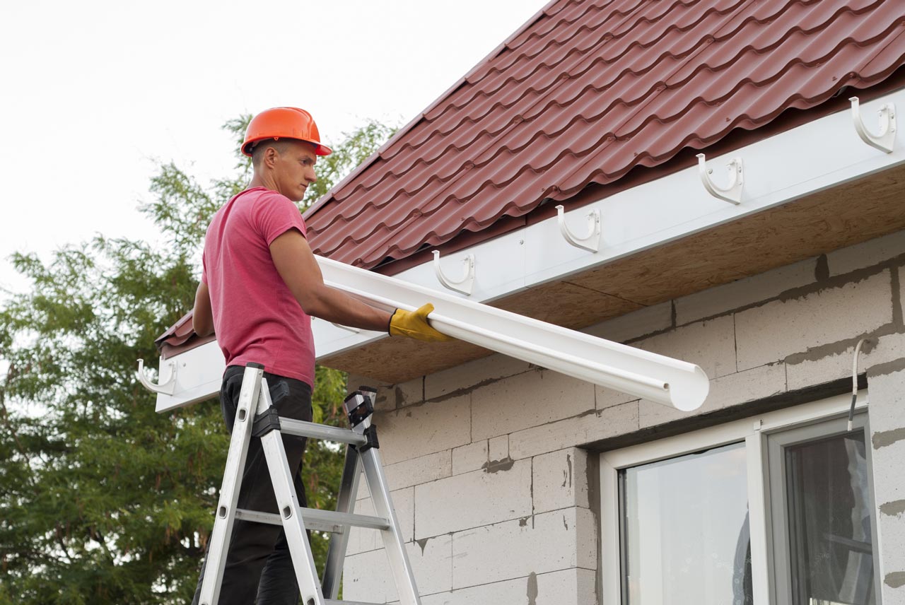 A skilled worker wearing hard hat and protective gloves while installing a gutter on a house