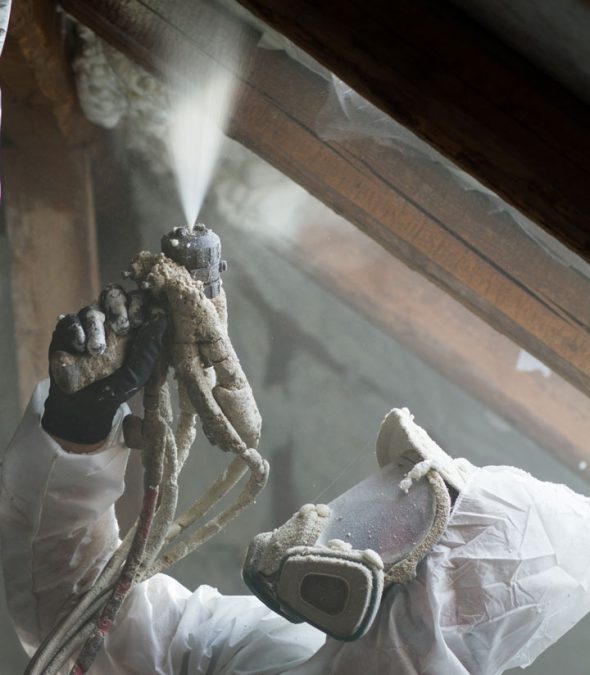 A worker on full protective gear doing spray foam insulation on an attic of a house