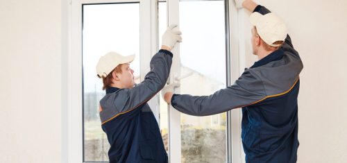 Two professional window installers carefully placing a frame for window replacement